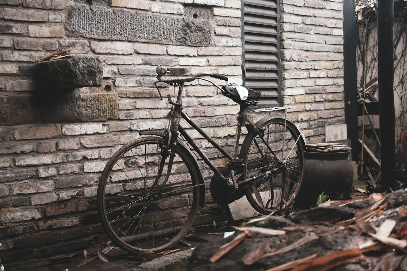 An old black bicycle leaning against a weathered brick wall
