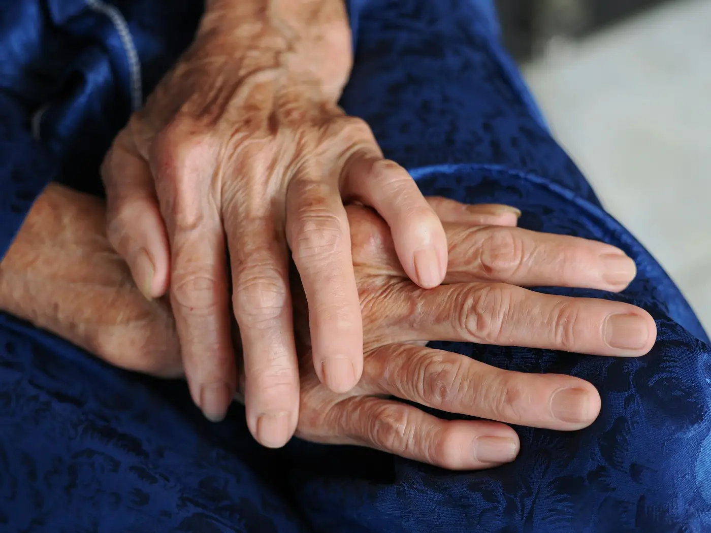 An elderly person's hands resting together on a blue jacket