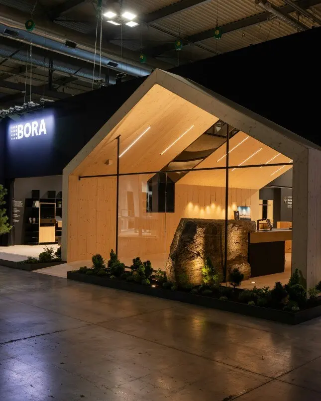 Bora’s stand seen from the aisle: a gabled timber house lit at night